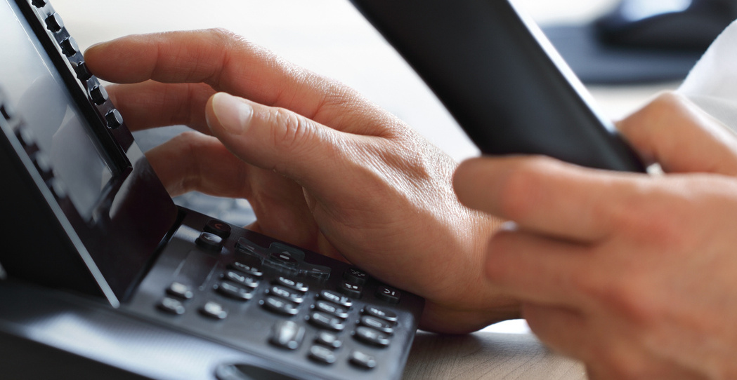 Person dialling a desk phone in a business office
